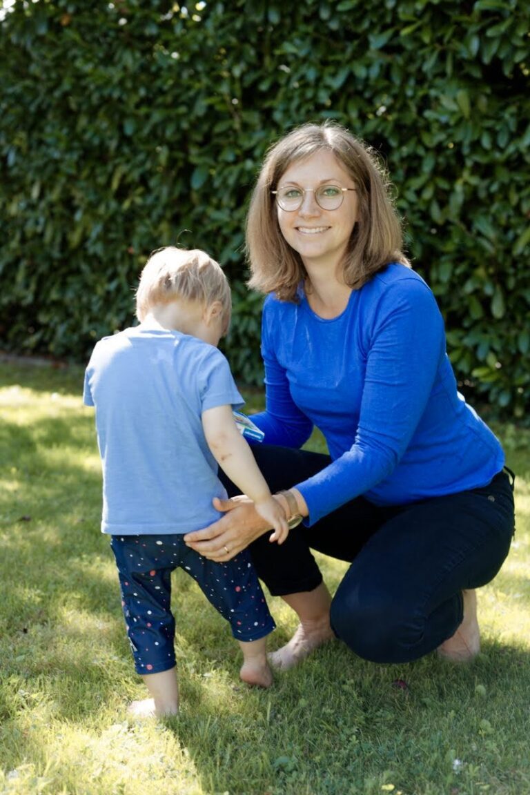 Caucasian woman kneeling next to a toddler and smiling at the camera