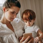Caucasian woman holding a toddler and looking at a phone