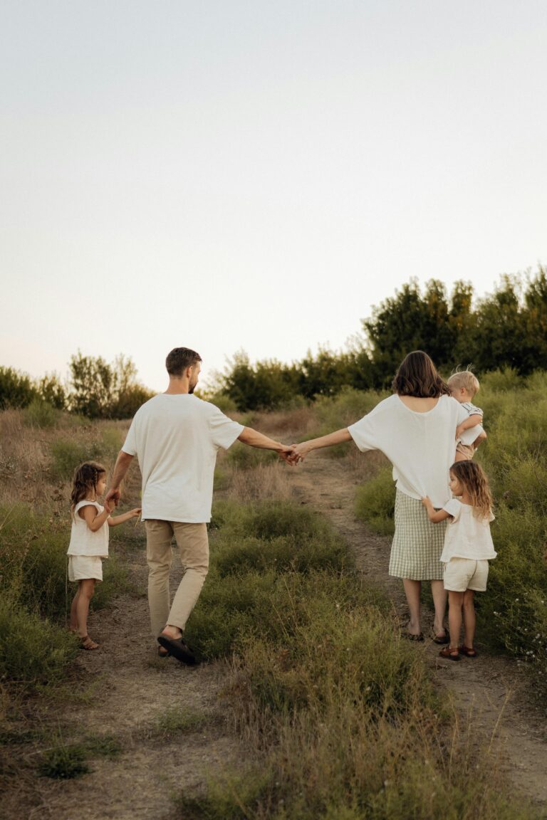 Caucasian family with three young kids holding hands and walking on a path - seen from the back.